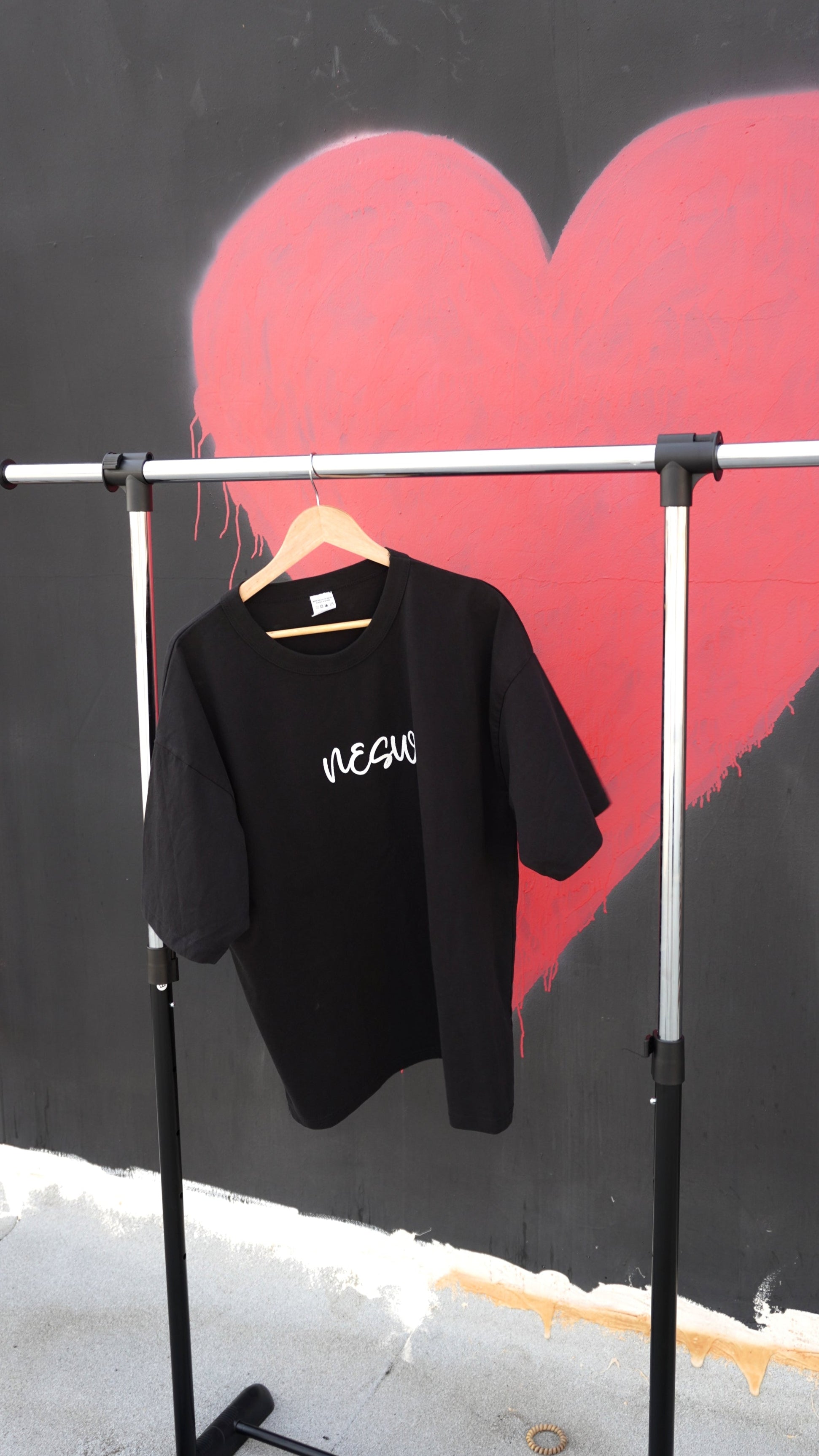 Black t-shirt with 'REBEL' text on a rack against a black wall with a red heart.