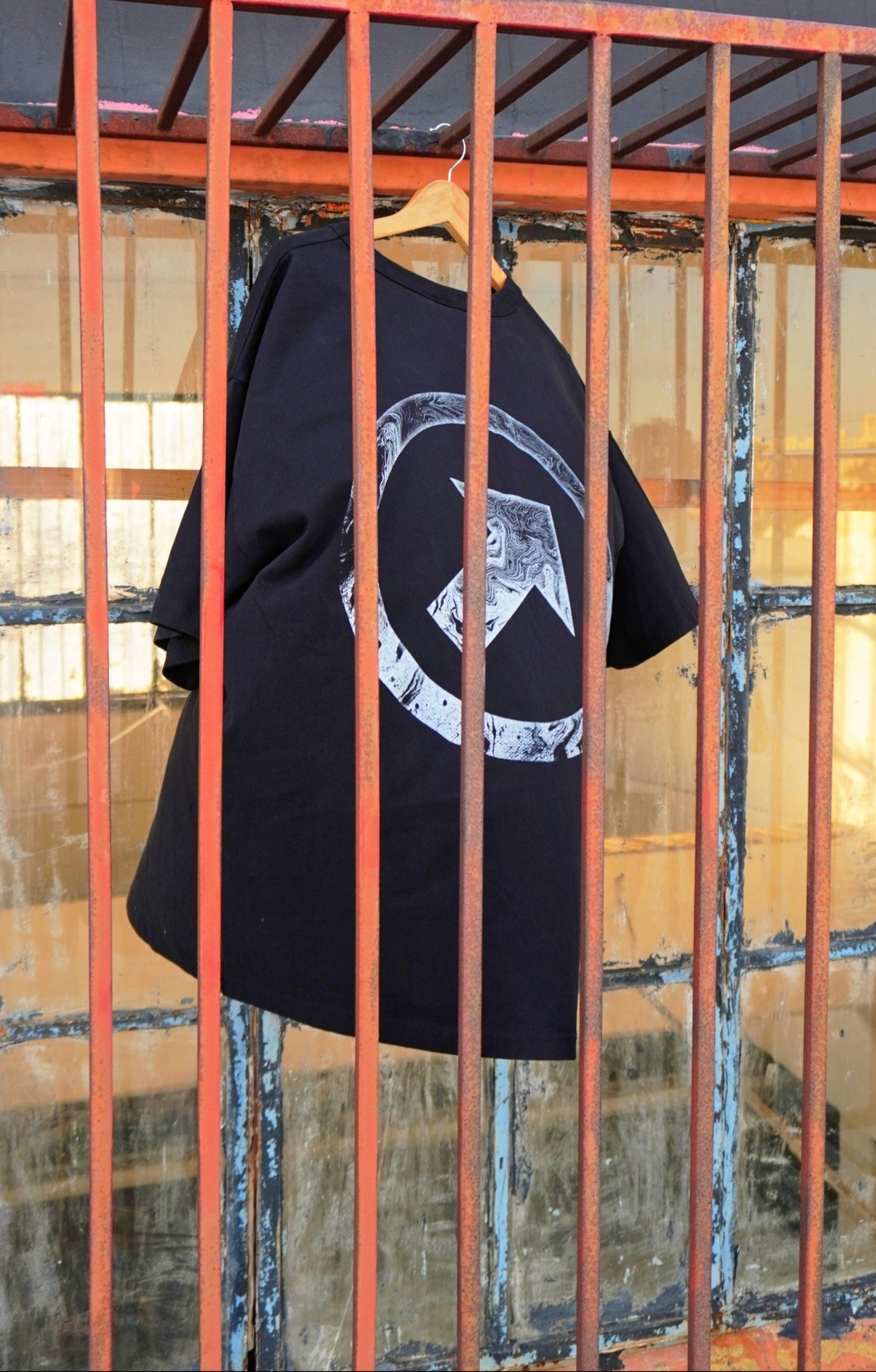 Black t-shirt with a white graphic design hanging on a red metal bar.